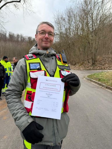Ein Mann in Warnkleidung hält ein Dokument in der Hand, umgeben von anderen Personen.